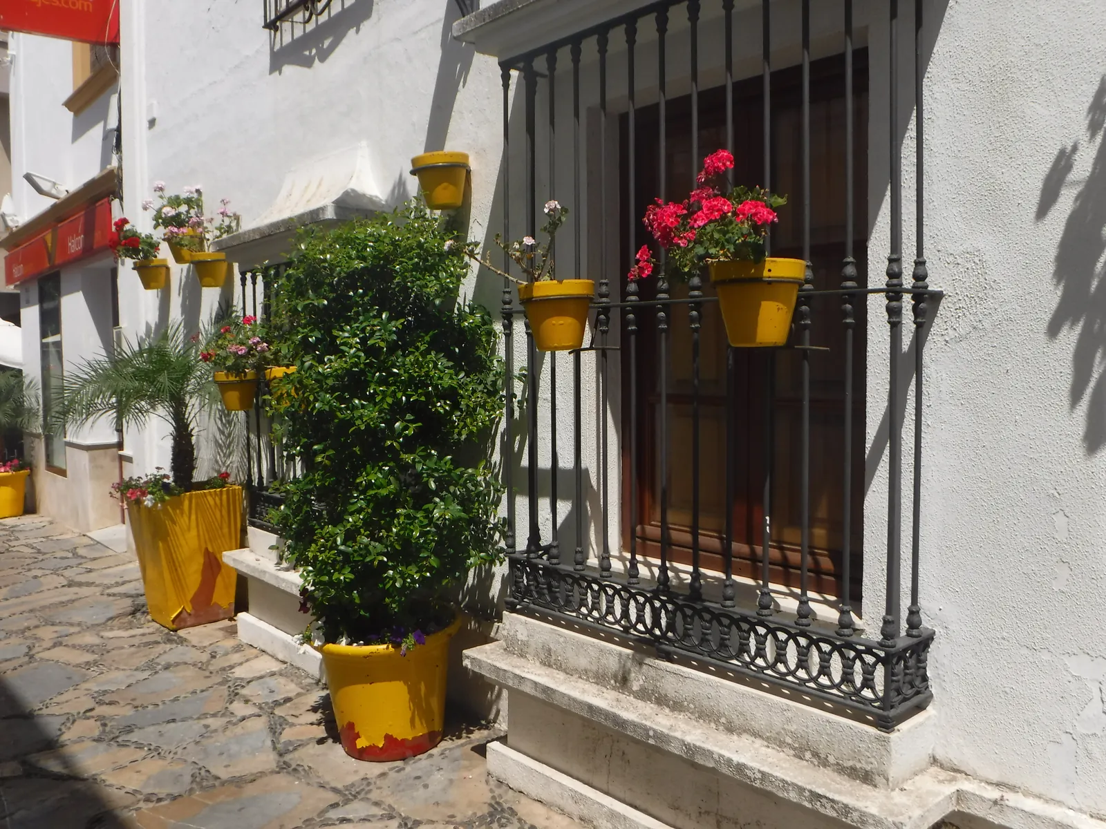 Calle blanca del casco antiguo de Estepona con macetas amarillas y geranios en las rejas de las ventanas